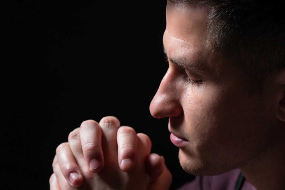 praying man on a black background shutterstock 1860530740
